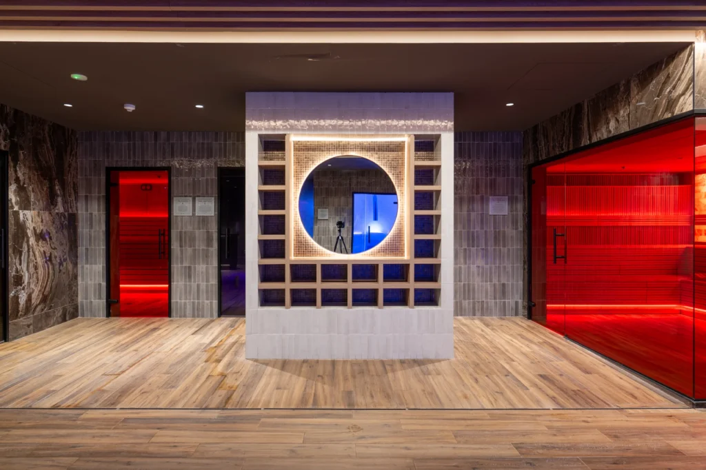 Zona de spa con saunas de cristal rojo y mueble central con ventana circular